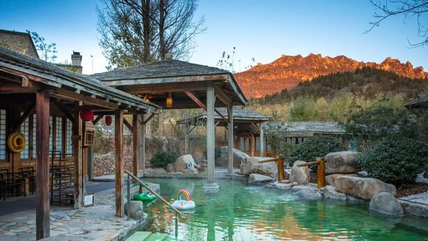 A rustic outdoor pool area with stone steps, wooden structures, and a mountain backdrop. - ATRIUM FENGZHU HOMESTAY (Miyun)