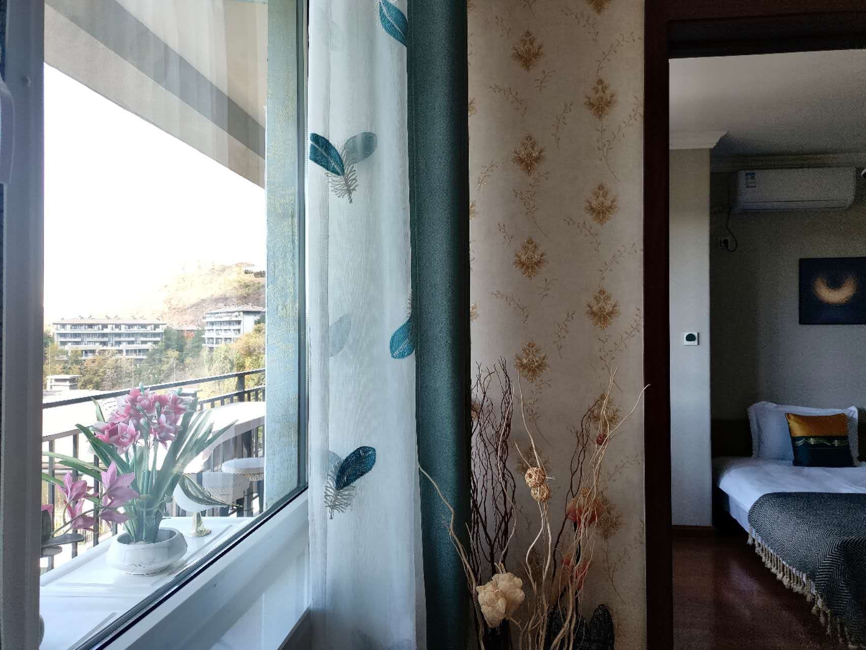 Une chambre d’hôtel avec un balcon, un lit recouvert d’une courtepointe bleue et blanche, et un mur orné d’un motif floral.