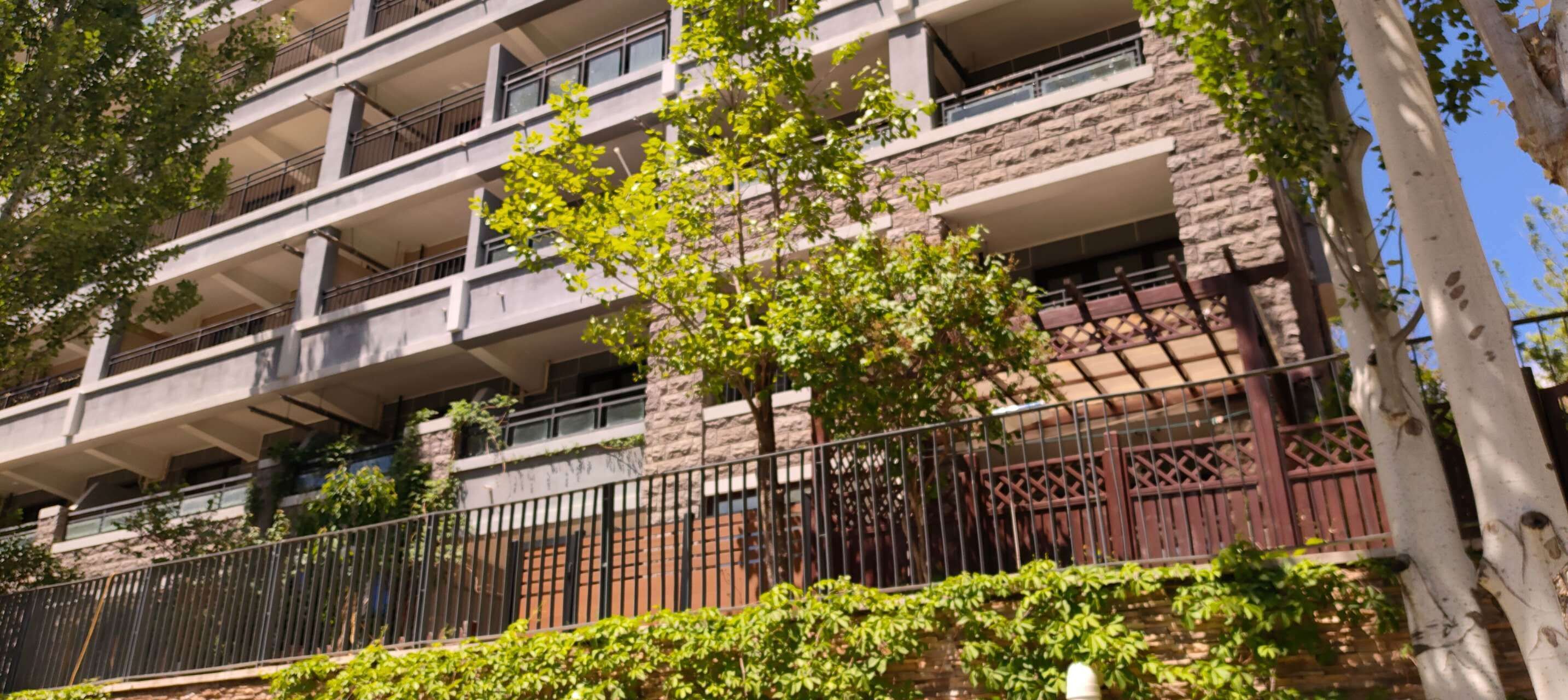 A multi-story building with balconies, a stone facade, and a metal fence.