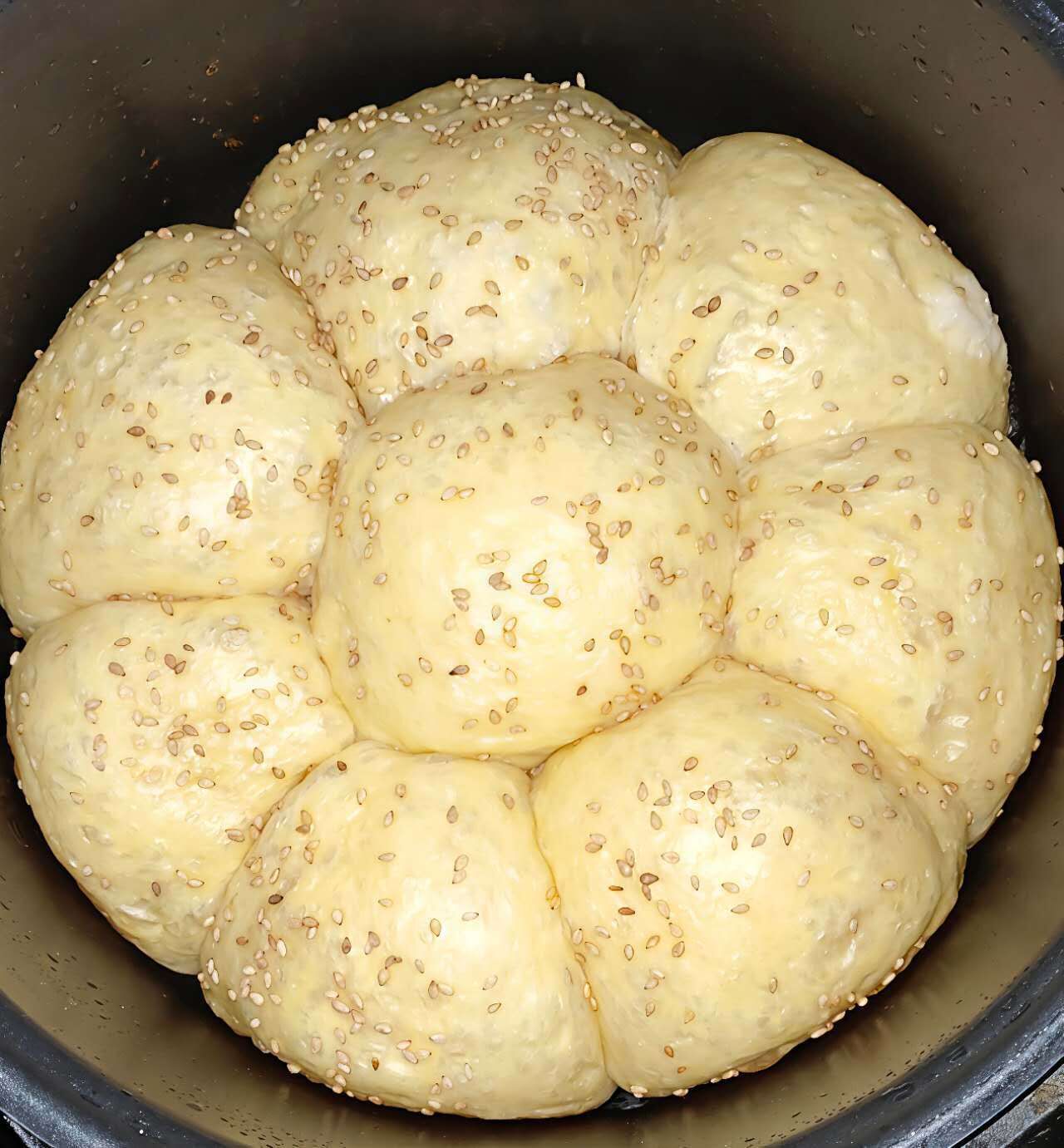 A pot containing several round, sesame-seed-topped bread rolls.