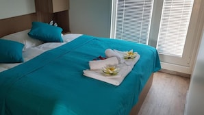 A neatly made bed with teal bedding and white pillows, a teal throw blanket, and a towel with a flower on it.