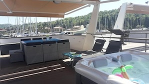A sunlit deck with a hot tub, lounge chairs, and a covered seating area with a pool table.