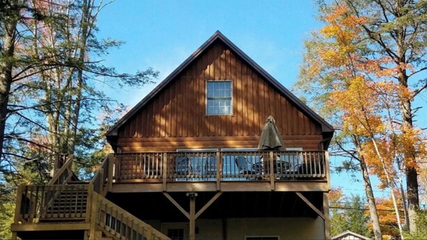 A two-story wooden cabin with a balcony, surrounded by trees.