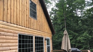 A wooden cabin with a deck, a table with chairs, and a covered grill area.
