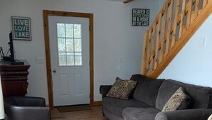 A living room with a grey sofa, a wooden staircase, a white door, and a patterned rug.