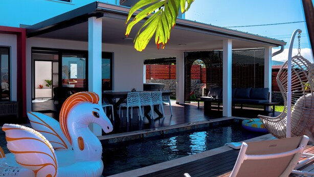 Un espace piscine extérieur moderne, doté d’un ensemble de mobilier de salle à manger et de chaises longues.