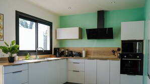 Une cuisine moderne avec des meubles blancs, un four noir de la marque Bosch, une fenêtre offrant une belle vue et un mur d’accent vert.