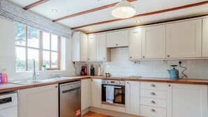 A kitchen with white cabinets, a dishwasher, an oven, and a window with a view of trees.