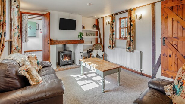 A cozy living room with a fireplace, leather sofas, a wooden table, and a TV mounted on the wall.