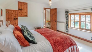 A bedroom with a bed, wooden wardrobe, a window with curtains, and a hanging light fixture.