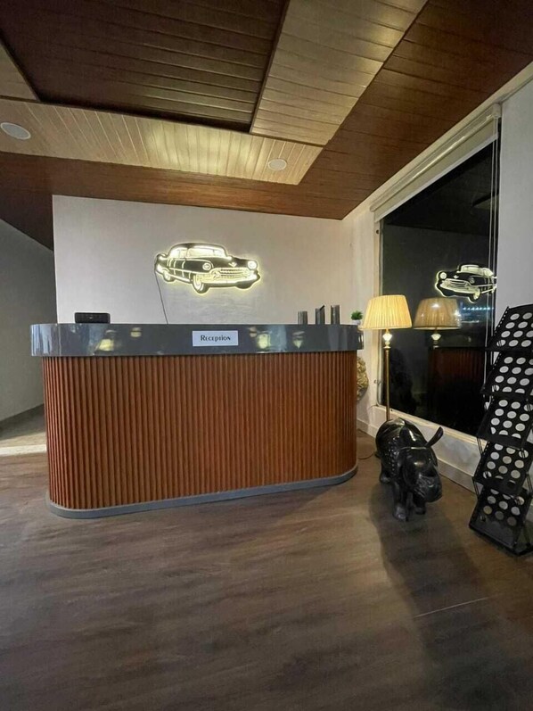 A reception desk with a 'Reception' sign, a car-shaped light fixture on the wall, and a bull statue next to a black polka dot display stand. - Royal Willow (Jogindarnagar)