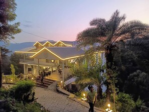 A house with a covered porch, steps leading up to the entrance, and a view of the surrounding landscape. - Royal Willow (Jogindarnagar)