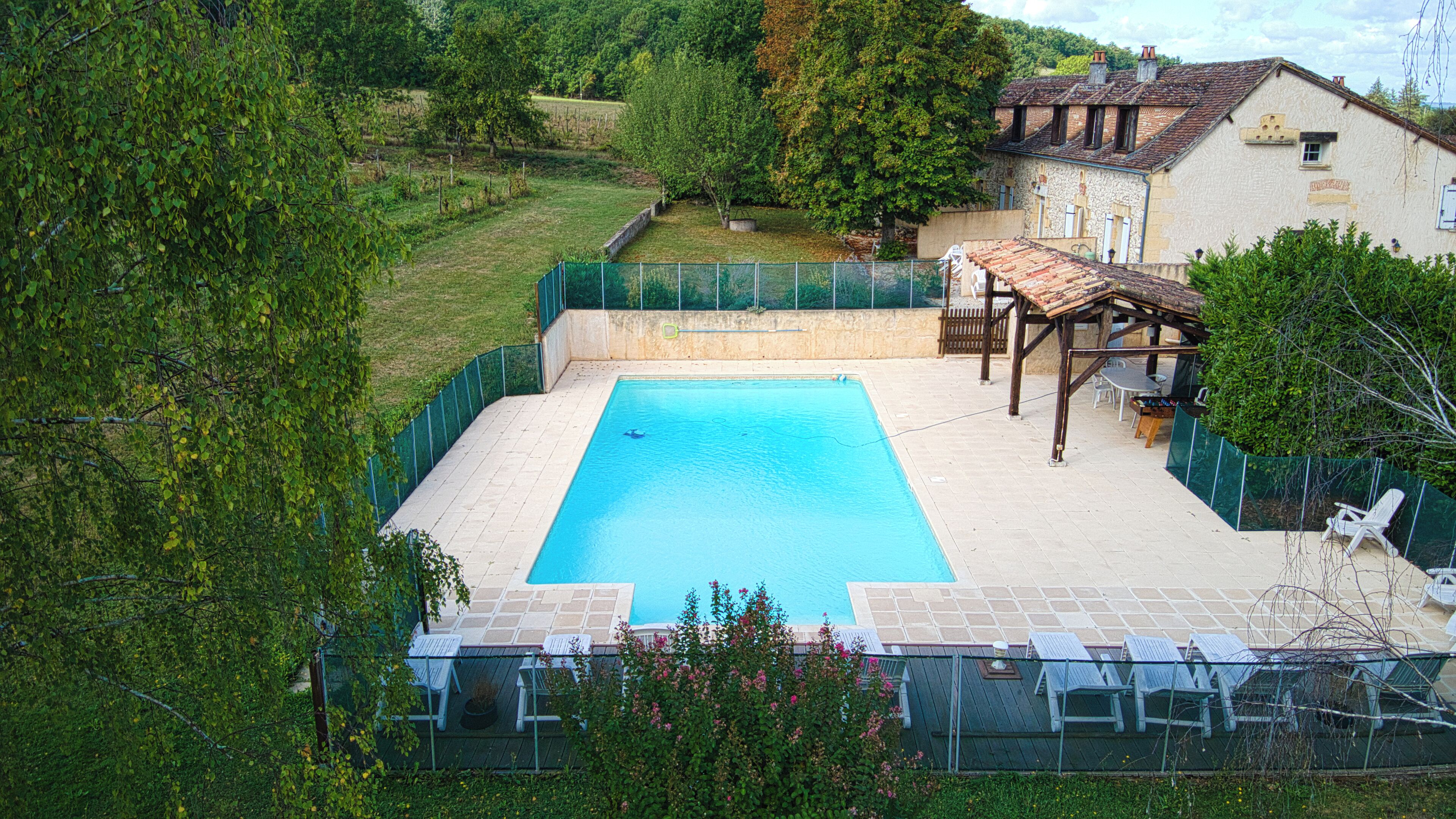 Une piscine rectangulaire avec une terrasse carrelée, entourée d’une clôture verte.