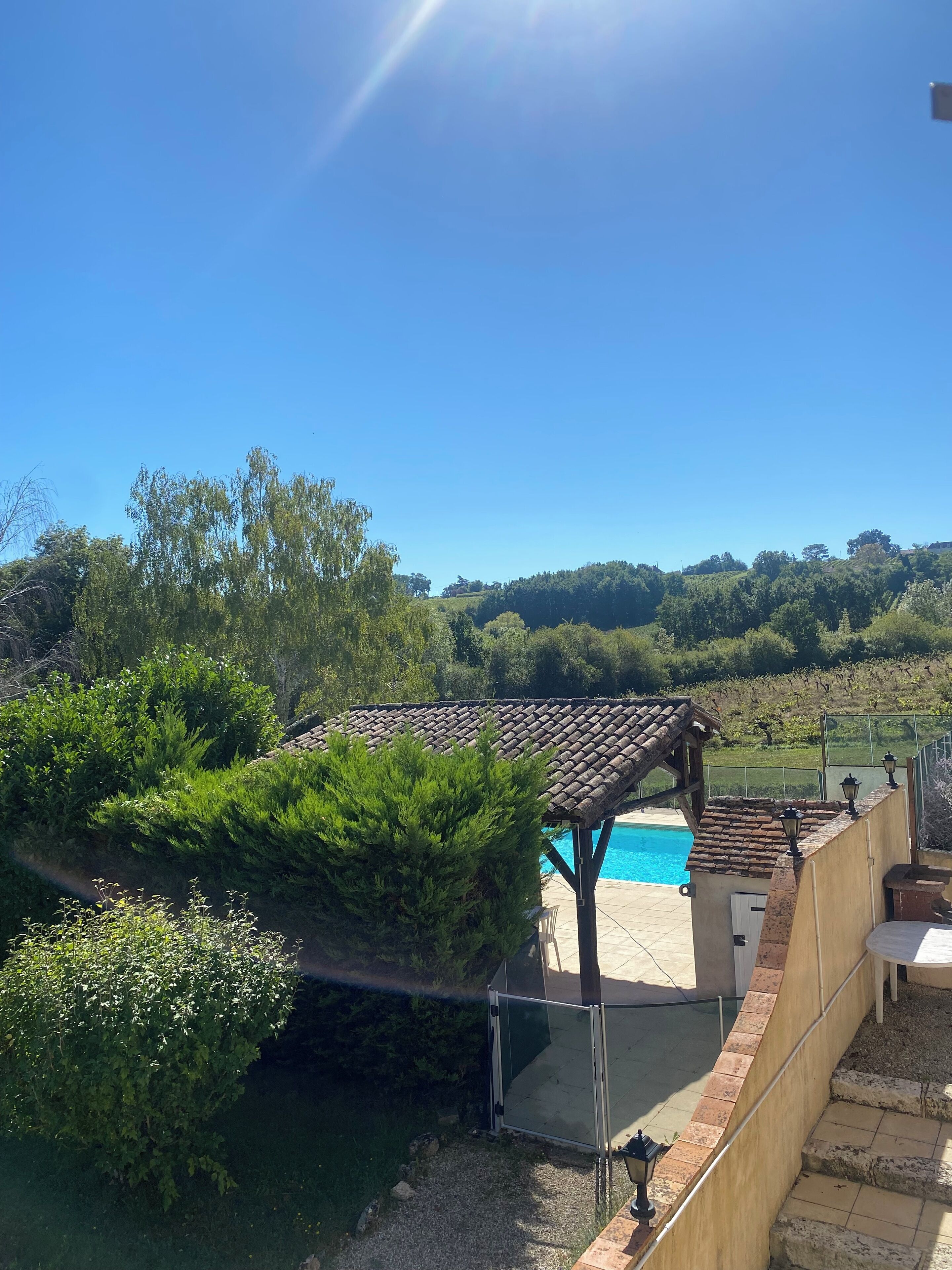Un espace piscine agrémenté d’une pergola, entouré d’une végétation luxuriante et offrant une vue sur les collines.