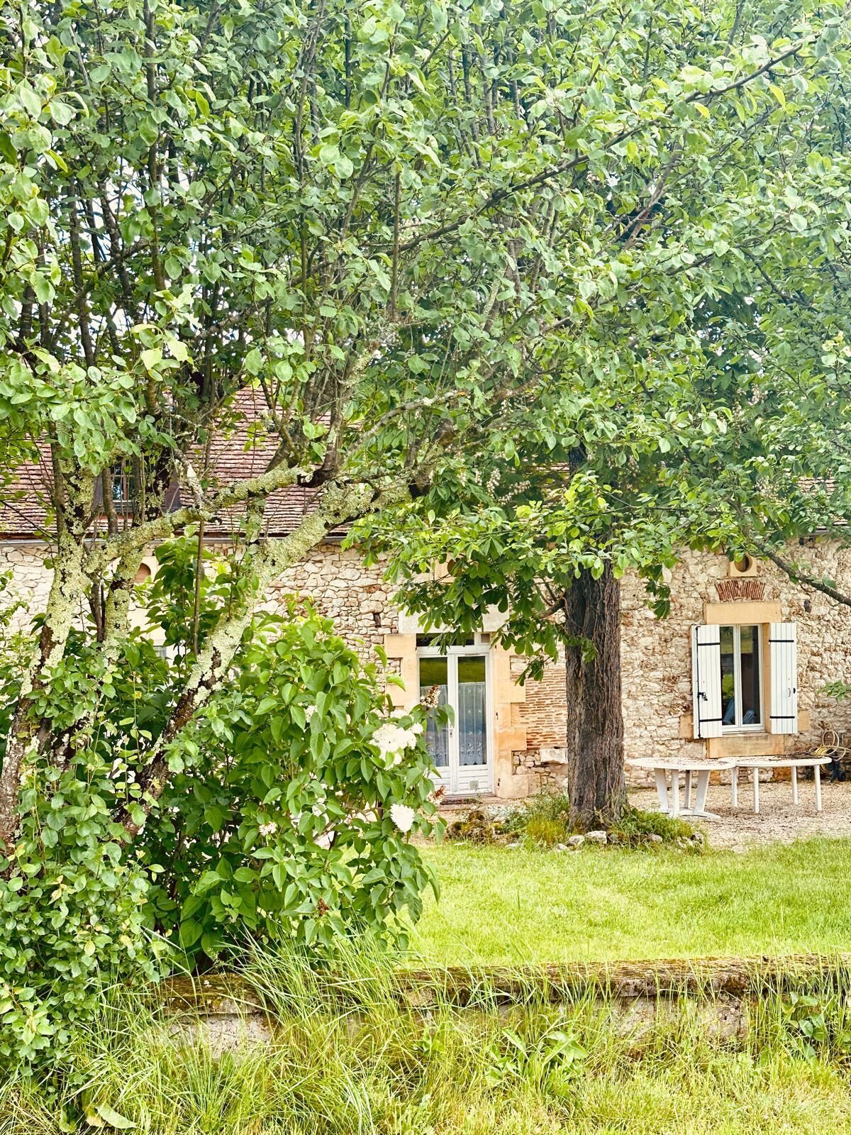 Ein Steinhäuschen mit rustikalem Charme, das eine Tür und Fenster mit Fensterläden zeigt, umgeben von üppigem Grün und einer Rasenfläche.