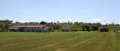 A rural landscape with a large open field, a farmhouse, and a small barn.