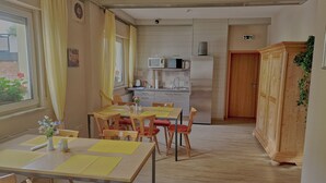 Een eethoek met een tafel en stoelen, een keuken met apparatuur, en een houten kast.
