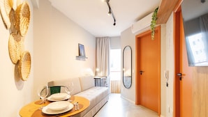 A modern living room with a sofa, dining table, and chairs. There is a large mirror on the wall and a door leading to another room. - Central Studium (São Paulo)