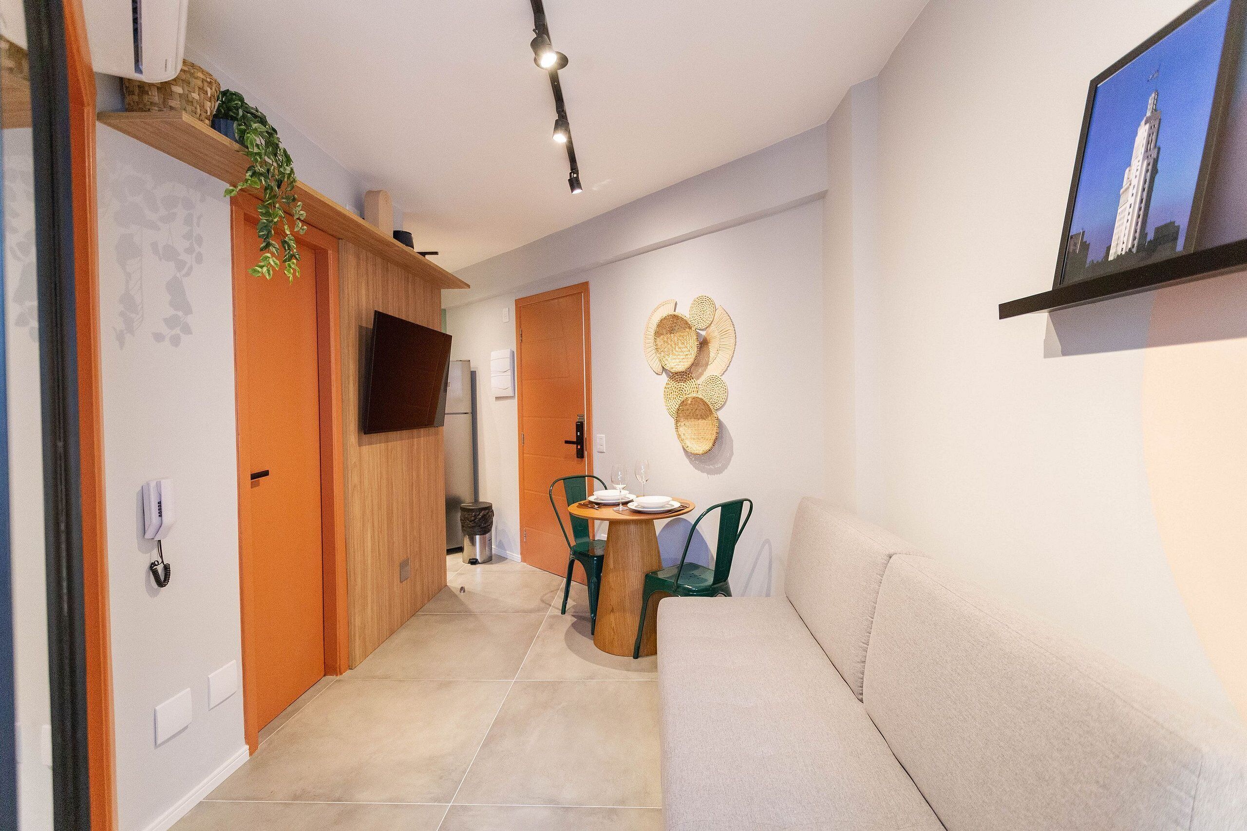 Un pasillo con un sofá, una mesa de comedor con sillas, un televisor montado y un adorno fijo en la pared.