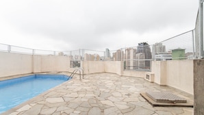 A rooftop swimming pool with stone flooring and a metal fence. - Central Studium (São Paulo)