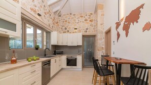Una cuina moderna amb parets de pedra, armaris blancs i una taula de menjador de fusta amb cadires negres.