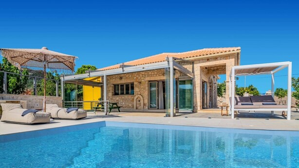 Zona de piscina amb una piscina blava cristal·lina, gandules i un espai de seients cobert.