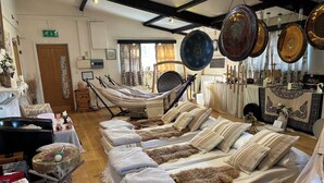 A room with a long bed, a hammock, and a table with decorative items. - Willow Cottage at Sound Healing Centre (Cardigan)