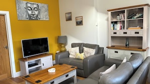 A living room with a sofa, a coffee table, a TV, and a bookshelf. - Willow Cottage at Sound Healing Centre (Cardigan)