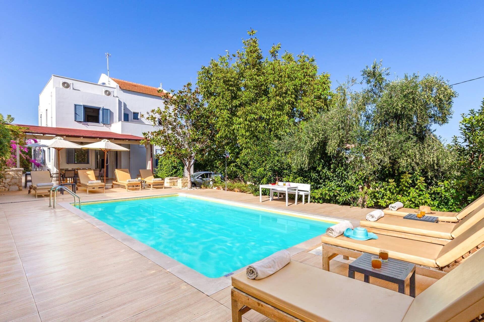 Un espace piscine avec des chaises longues, une table et un bâtiment en arrière-plan.