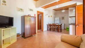 Un salon avec un téléviseur, un meuble en bois et un canapé. Il y a également un coin repas avec une table et des chaises.