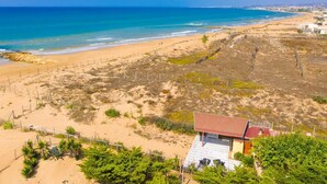 Une plage avec vue sur la mer, une zone délimitée par une clôture, un petit bâtiment avec un toit rouge et un ciel bleu dégagé.