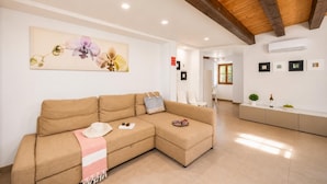 Una sala de estar con un sofá, un cuadro y una zona de cocina con mostrador y planta.