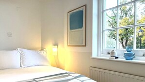 Quarto de hotel com cama, mesa de cabeceira com abajur, janela com vista para árvores e radiador.