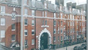 Vista de um edifício de tijolos vermelhos com uma grande entrada em arco, várias janelas e uma rua em frente.