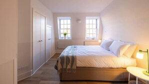 Ein Schlafzimmer mit einem Bett, einem Nachttisch und zwei Fenstern.