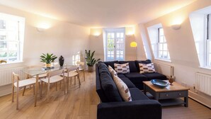 Ein modernes Wohnzimmer mit einem Glastisch, einer schwarzen Couch und einem kleinen Holztisch.