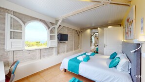 A bedroom with a large bed, a TV mounted on the wall, and a window with a view of the outdoors.