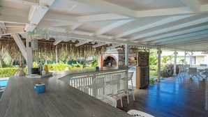 An outdoor bar area with a pool, white chairs, and a tiki bar.