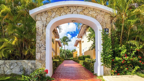 A pathway leading through a stone archway surrounded by lush greenery and palm trees. - Oasis Cocotal: Family 4BR Apartment in Punta Cana (Punta Cana)
