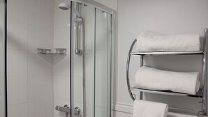 Een douche met glazen wanden, een chromen kraan en een witte handdoekhouder met opgevouwen handdoeken.
