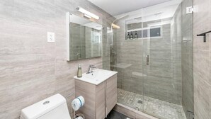 Um banheiro moderno com chuveiro envidraçado, pia branca e toucador com espelho.