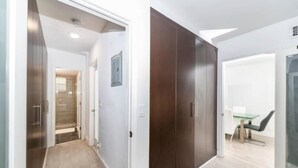 Corredor que leva a um quarto com porta de vidro, armário de madeira e área de refeições com mesa e cadeiras.