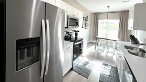 Una cocina moderna con electrodomésticos de acero inoxidable, armarios blancos y un amplio ventanal que proporciona luz natural.