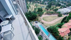 A high-rise building with a rooftop pool, outdoor seating, and a view of a park and residential area. - Sandtoncity-apartment-sleeps2-pool-parking (Johannesburg)