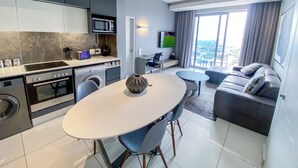 A modern kitchen with a dining area, a flat-screen TV, and a sofa with a city view. - Sandtoncity-apartment-sleeps2-pool-parking (Johannesburg)