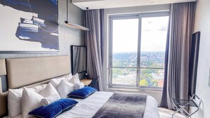 A hotel room with a large bed, a city view, a flat-screen TV, and a modern design. - Sandtoncity-apartment-sleeps2-pool-parking (Johannesburg)