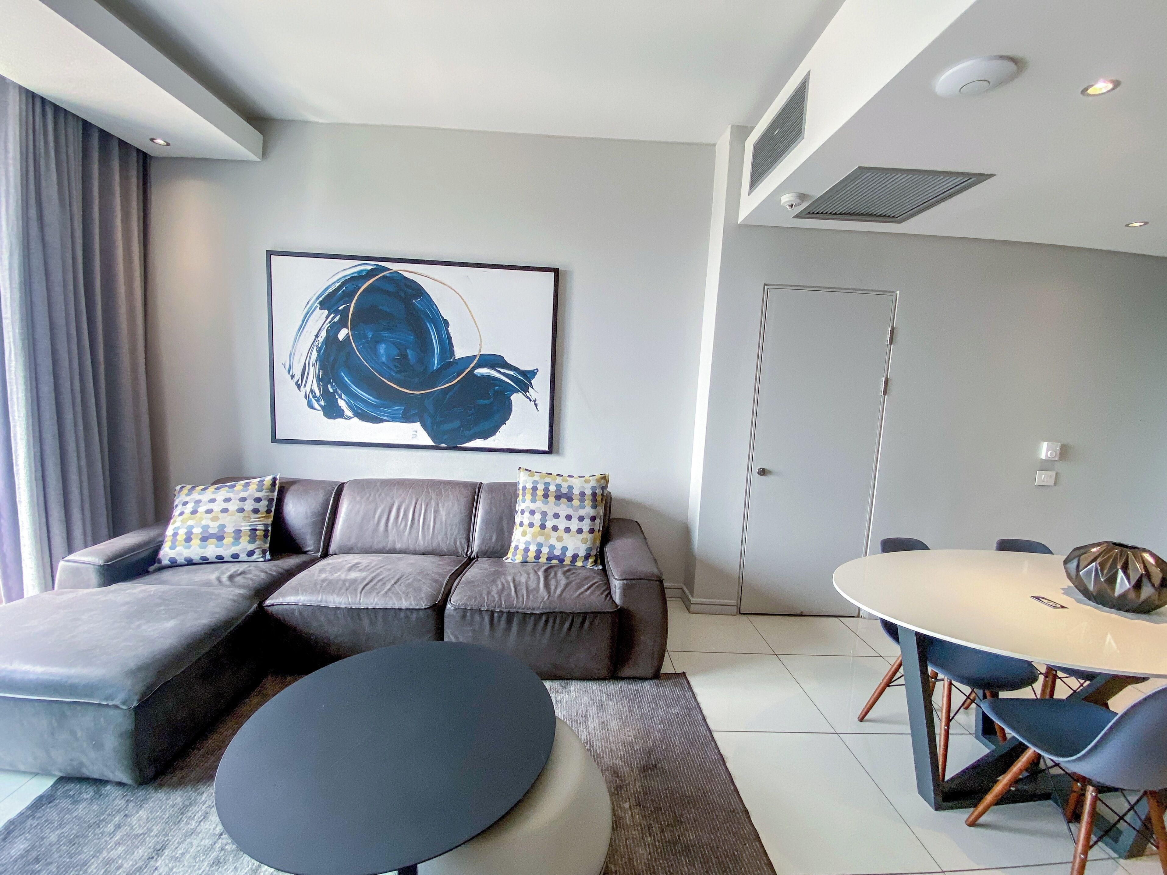 A modern living room with a grey sofa, a round coffee table, and a dining table with chairs.