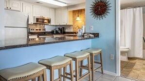 A modern kitchen with white cabinets, a granite countertop, and a sun-shaped wall decoration. There are three wooden stools at the counter.