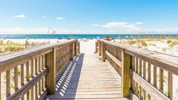 A wooden boardwalk leading to a beach with clear skies.