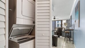 A laundry room with a front-loading washer and dryer, a trash can, and a small table with chairs.